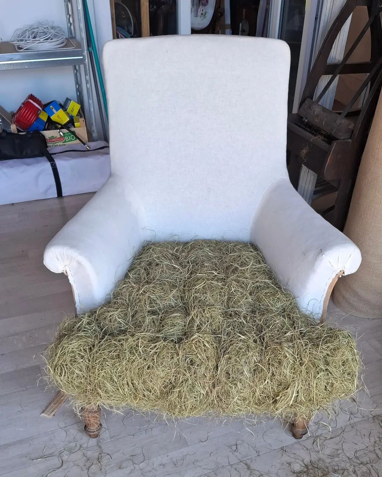 Fauteuil à dossier haut recouvert de toile blanche, assise garnie de crin végétal en cours de piquage